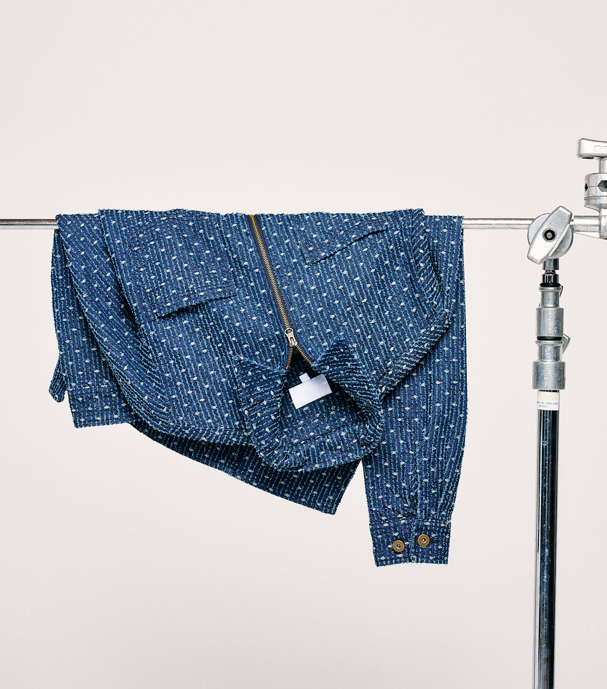 A blue patterned jacket draped over a metal stand against a plain light background.